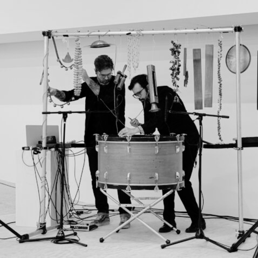 Image en noir et blanc du duo Catalão–Thibault. On voit les deux hommes penchés sur des instruments à percussion. La photo est en noir et blanc.